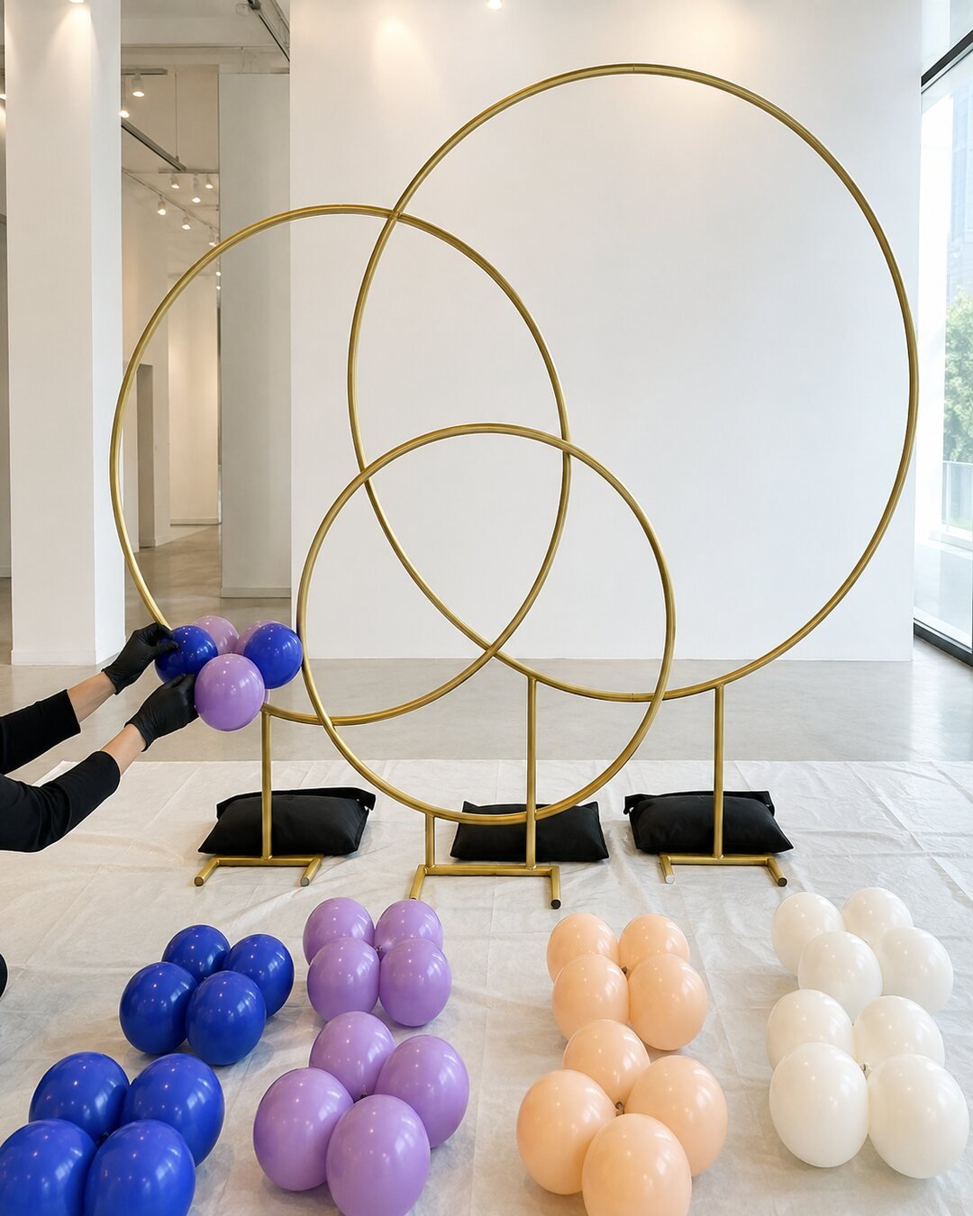 Decorator attaching cobalt and orchid balloon quads to three safely weighted gold orbit rings