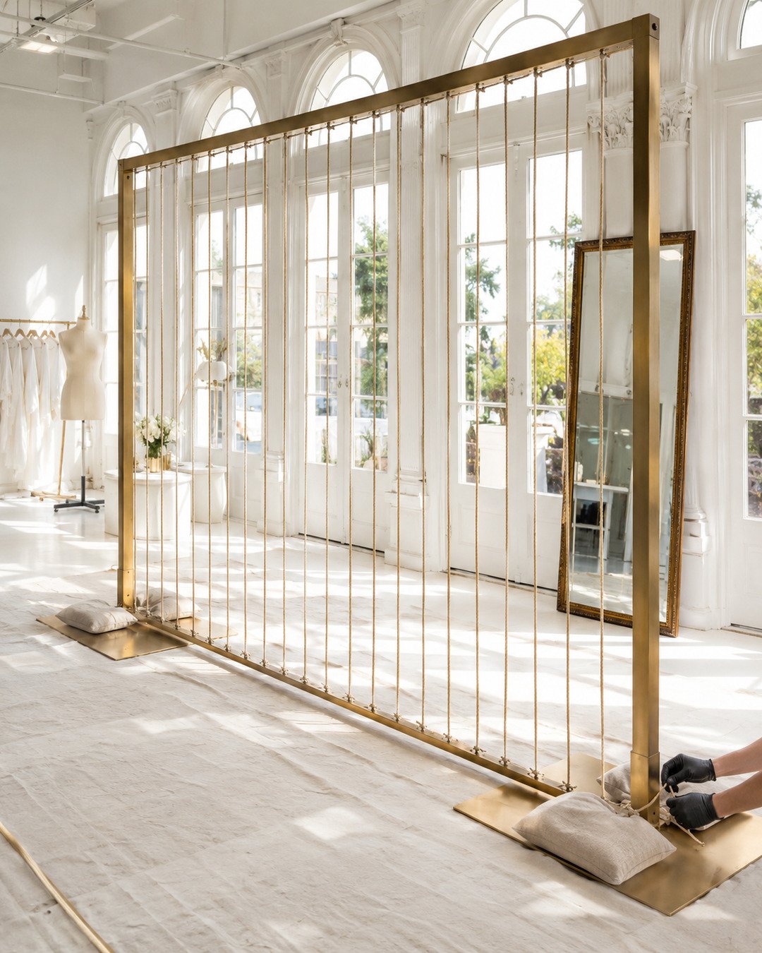 Freestanding brass loom frame with evenly spaced vertical cords while gloved hands secure weighted base plates.