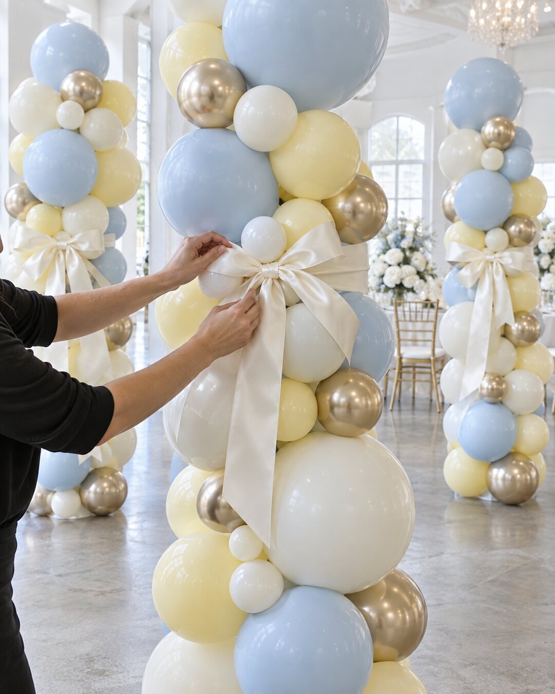 Elegant powder-blue, ivory, butter-yellow and champagne-gold balloon column finished with an ivory satin bow