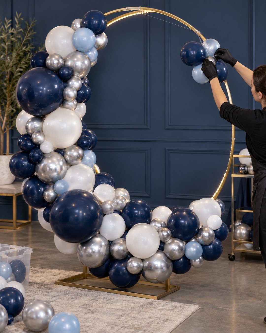 Decorator attaching navy white silver and icy-blue balloon clusters to a crescent moon frame while preserving the glowing inner curve
