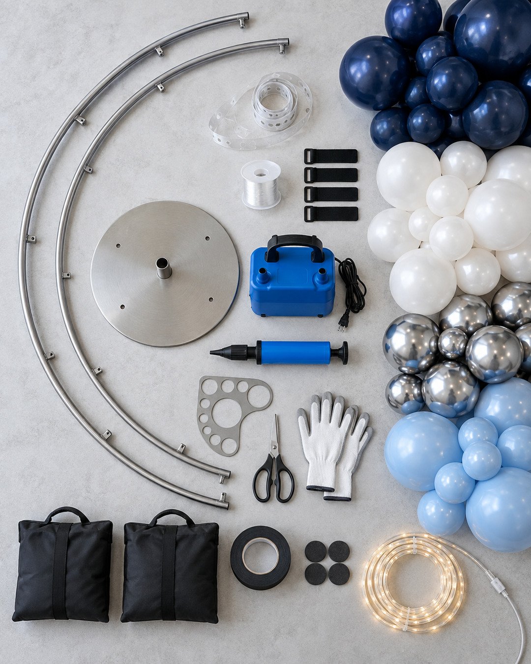 Crescent moon frame, weighted base, balloon pumps, sizing tool, navy white silver and blue balloons, ties, tape, gloves and LED rope arranged on a worktable