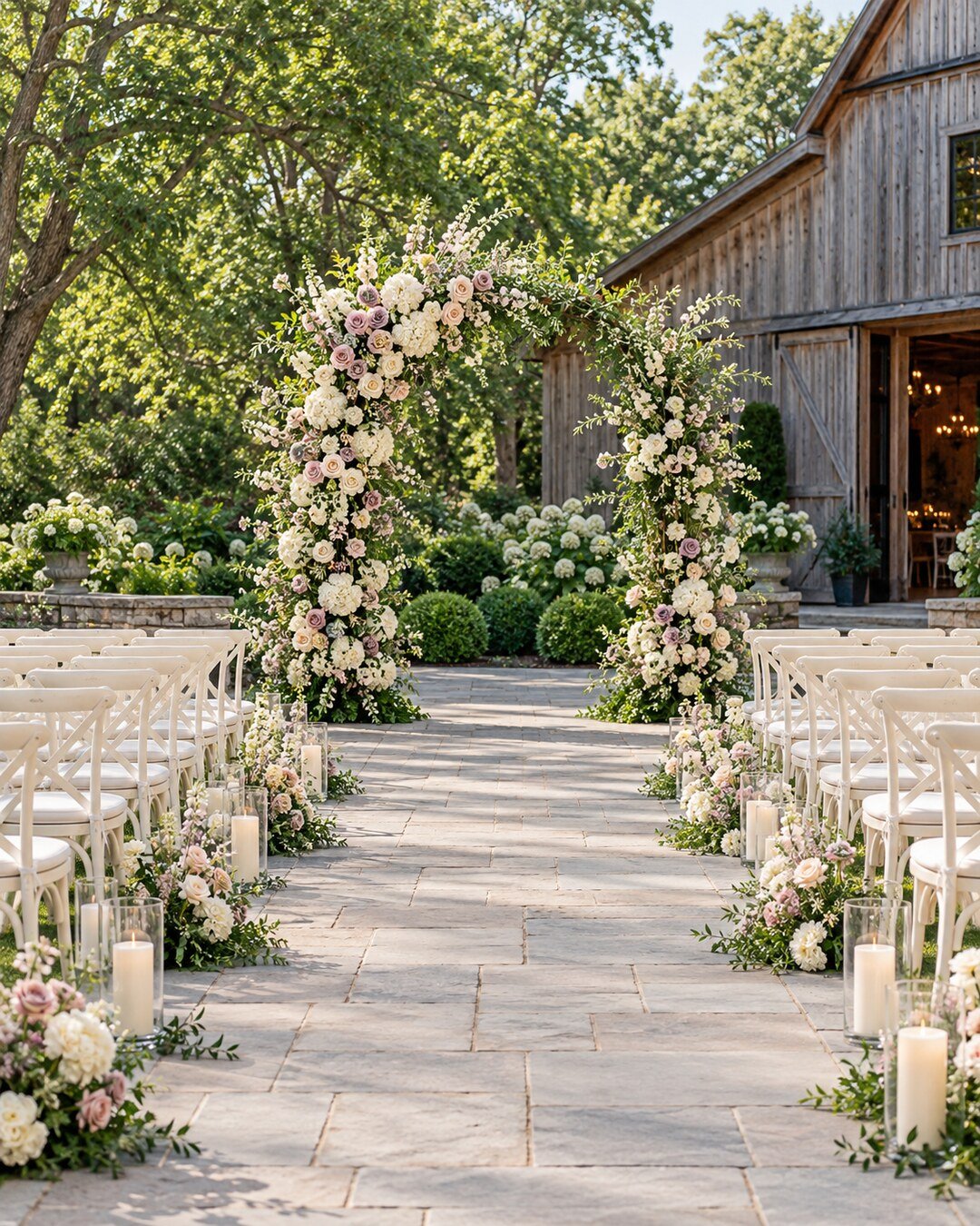 Elegant garden-barn wedding ceremony with a weighted floral arch, ivory chairs, low aisle flowers and flameless candles