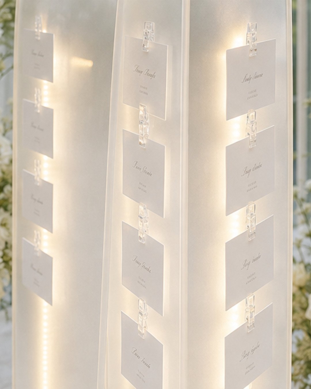 Close detail of ivory escort cards clipped to glowing layered translucent sail panels
